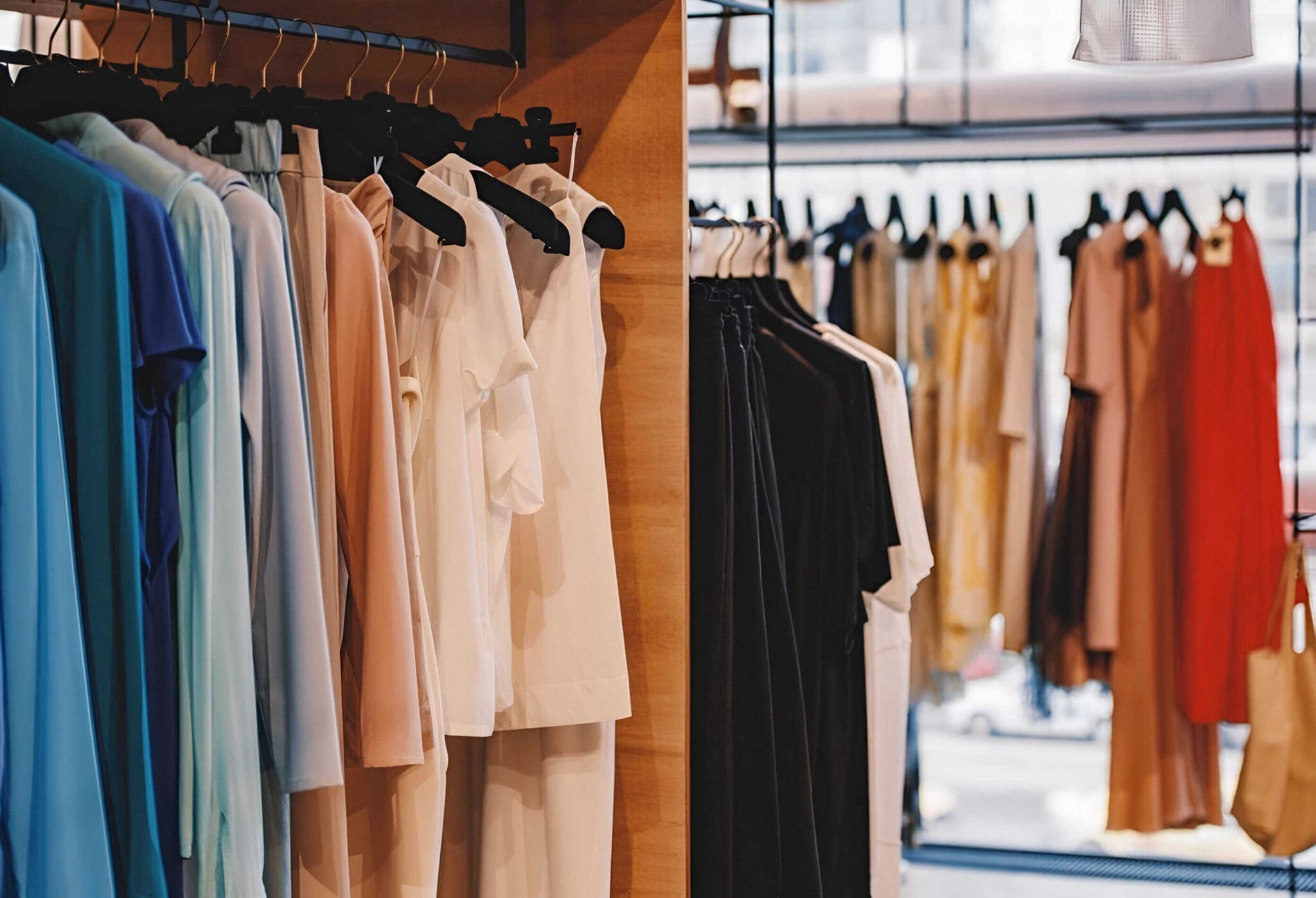 A clothing store display showcasing a variety of neatly arranged garments on hangers, featuring light-colored shirts and blouses on the left and earth-toned pants and dresses on the right.